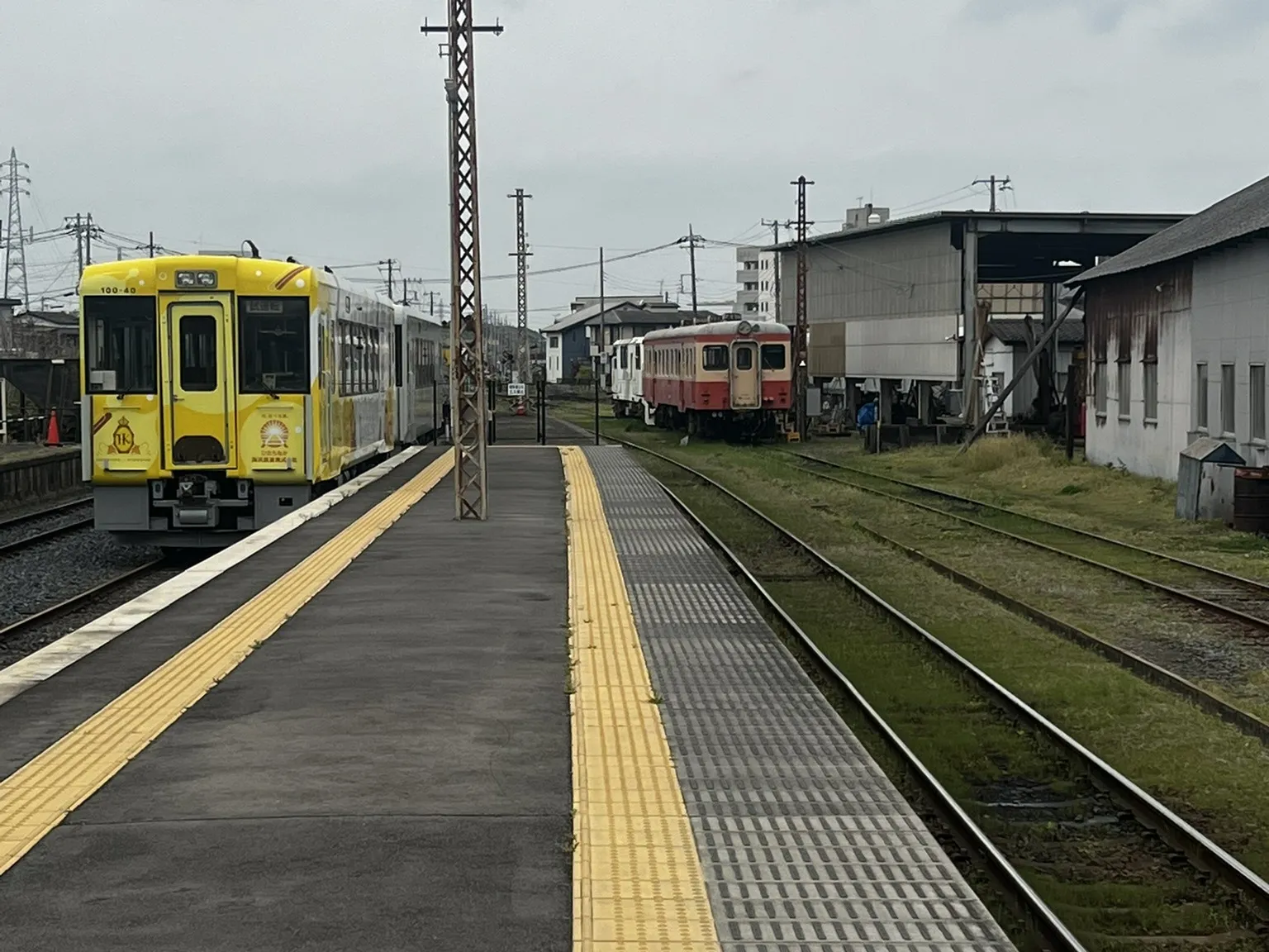 A quiet station platform with a yellow train on one track and an old red-and-cream train on the other